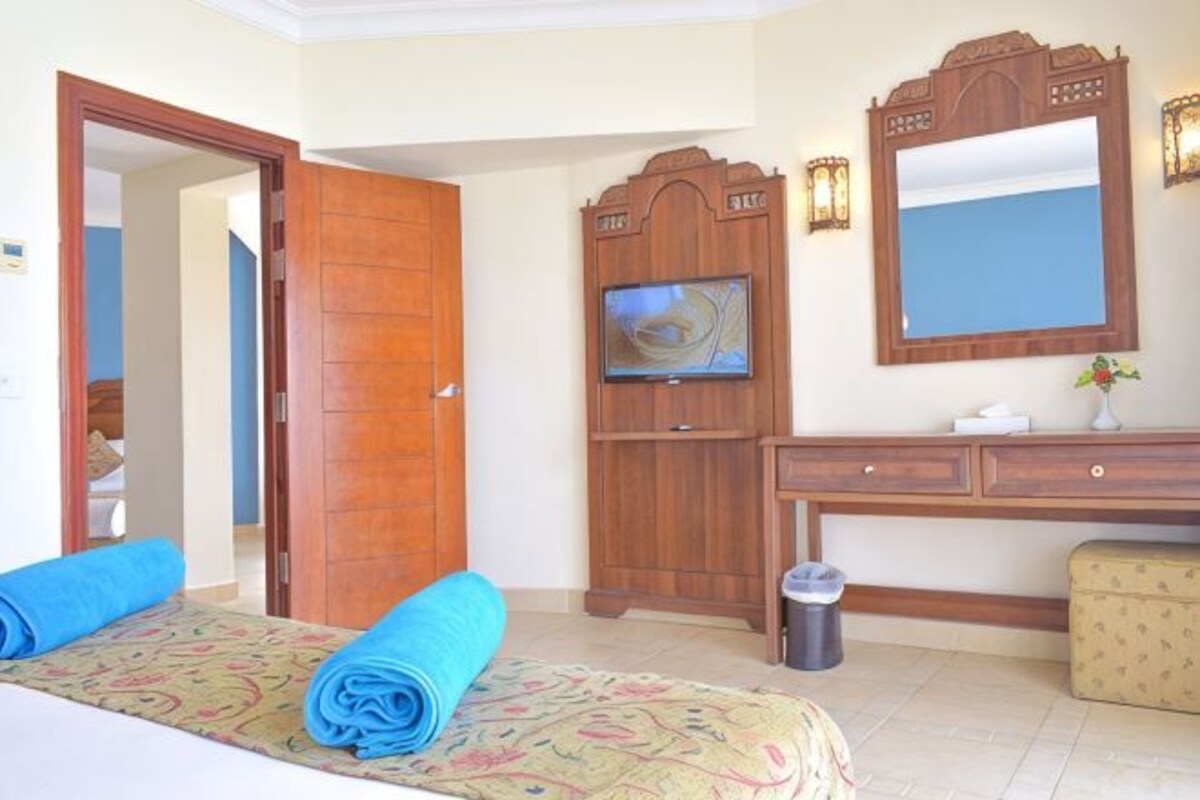 Une chambre d’hôtel avec un lit, une armoire en bois, une télévision et un bureau avec un miroir.