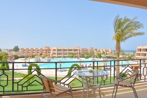 A balcony with a view of a swimming pool, palm trees, and hotel buildings. - Jasmine Palace Resort & Spa (Hurghada)
