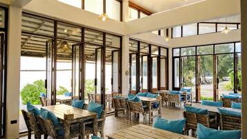 Un comedor interior espacioso con mesas y sillas de madera, ventanas amplias y lámparas colgantes.