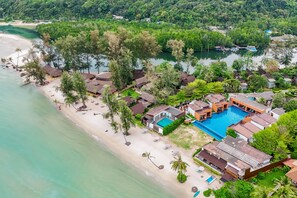 Vista aérea de un resort con playa, piscina y abundante vegetación.