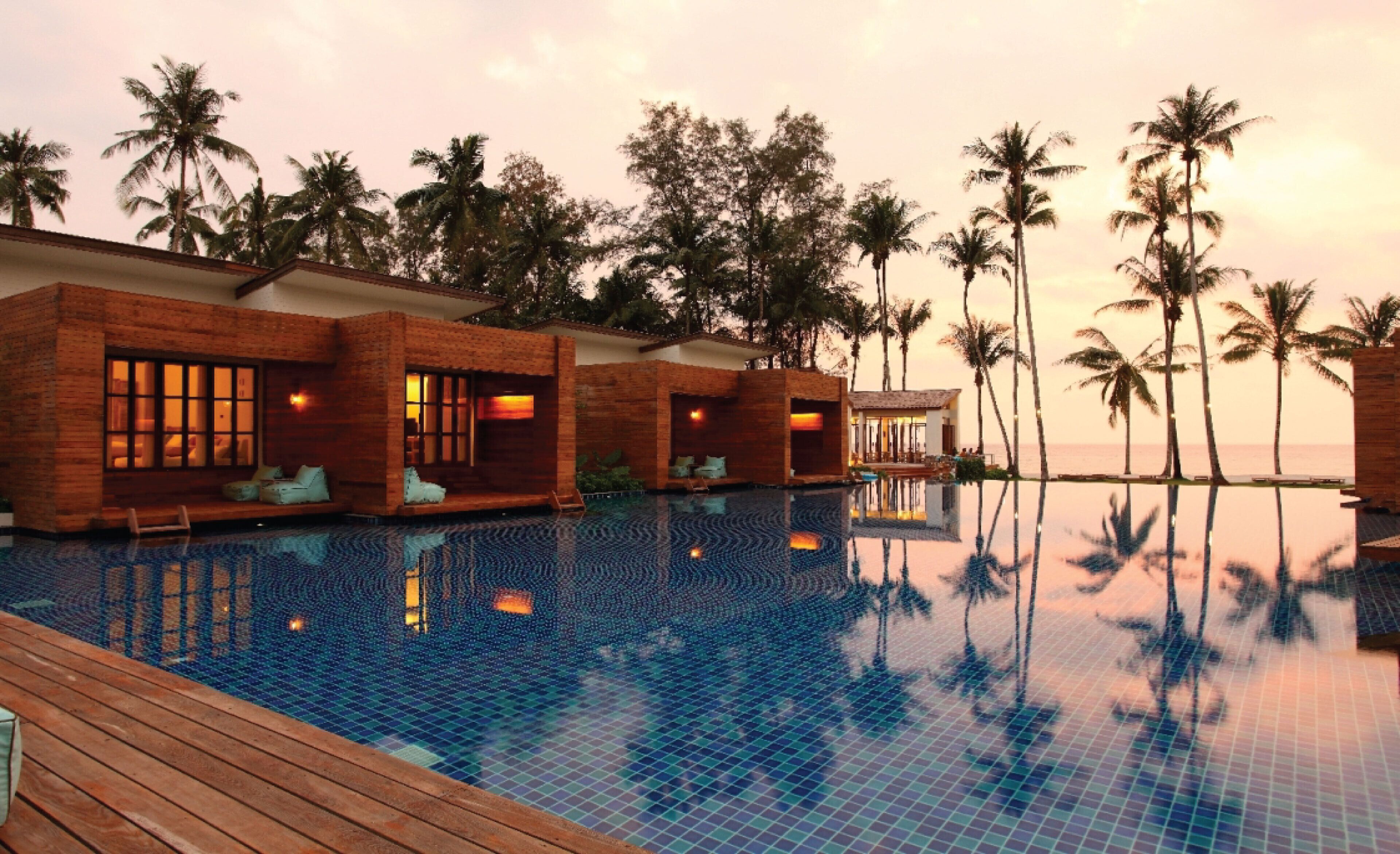 Un resort con piscina, terraza de madera y palmeras.