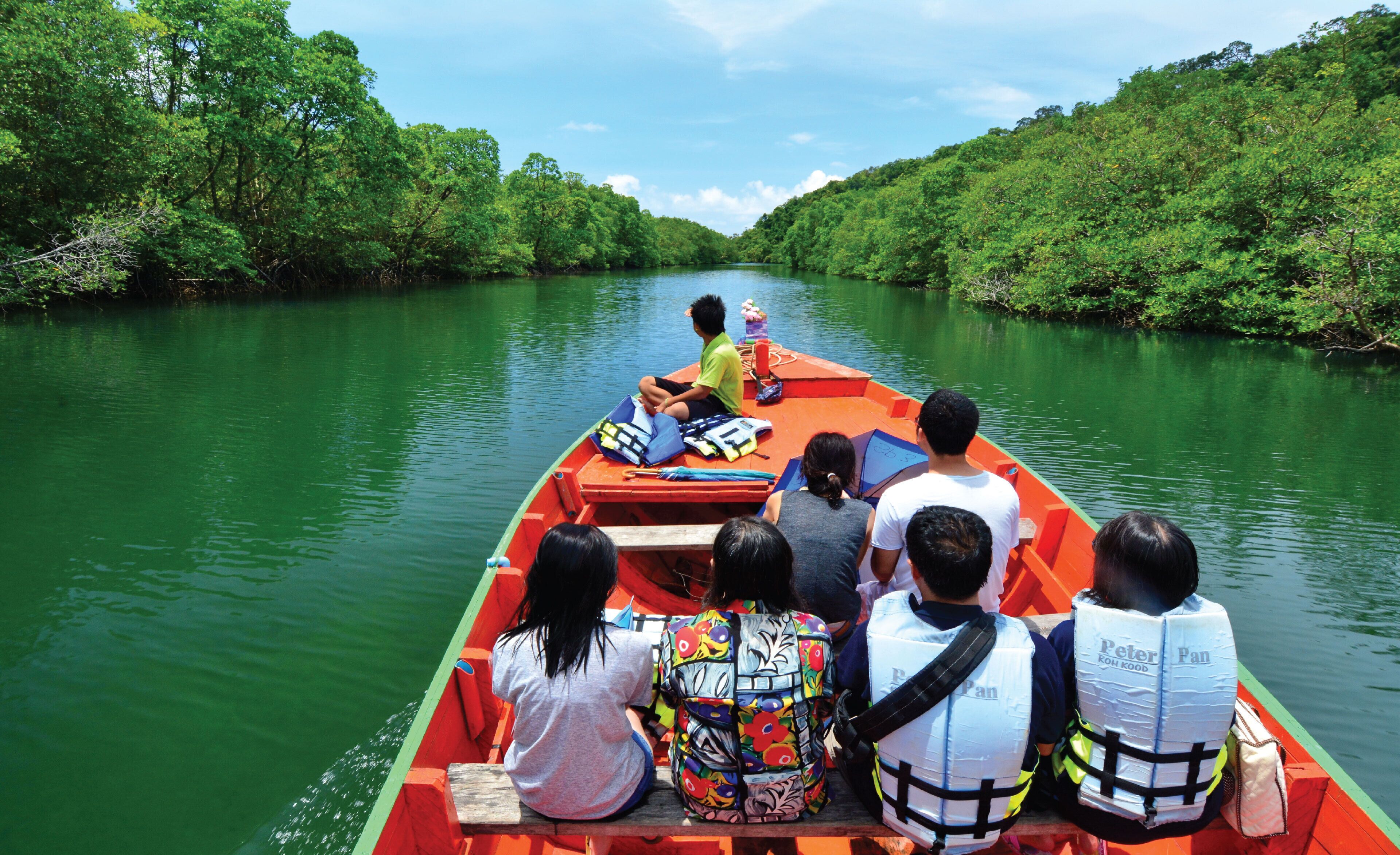 A group of people on a narrowboat with life jackets, navigating a narrow green river surrounded by dense greenery.