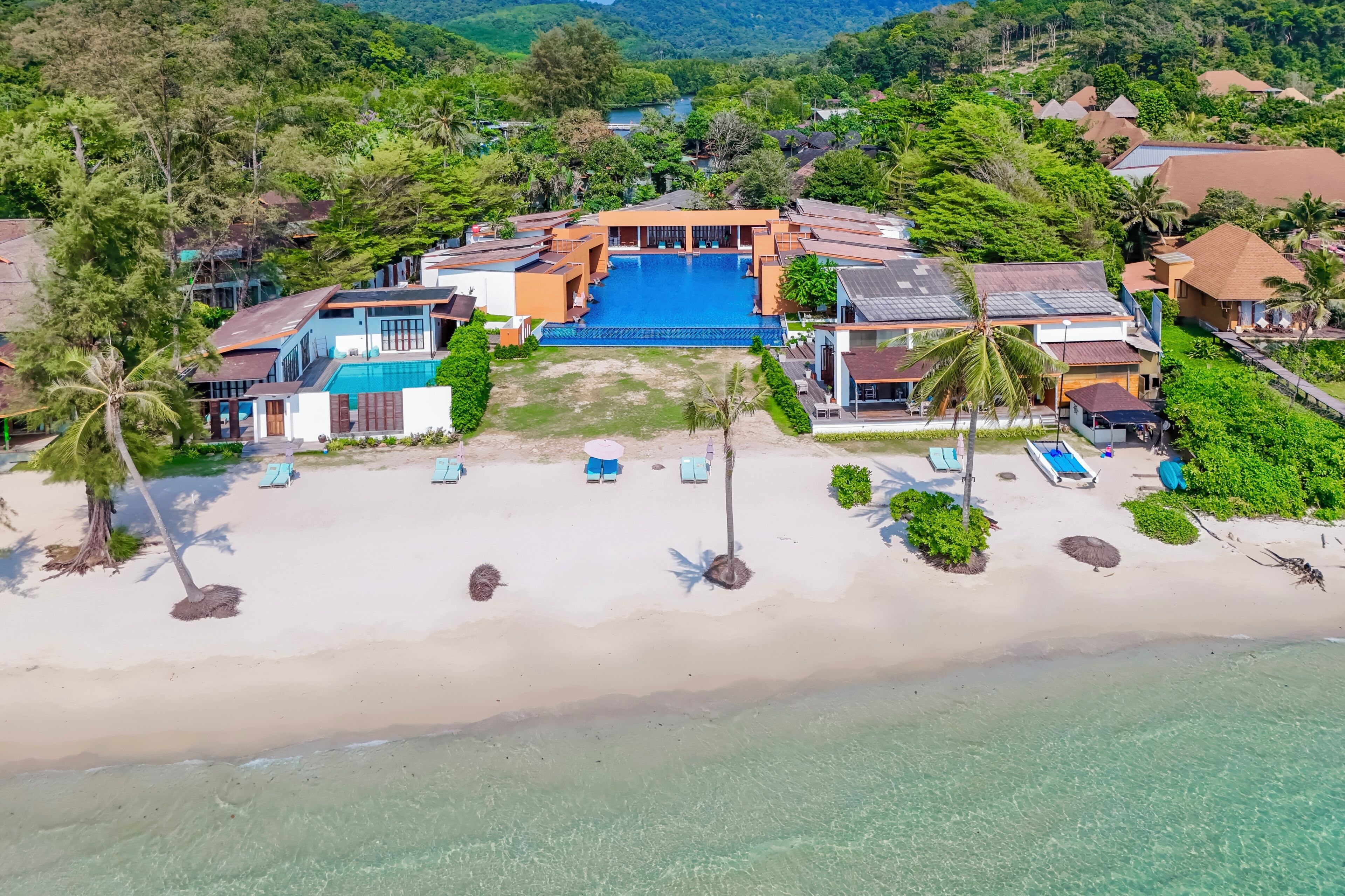 An aerial view of a resort with a swimming pool, beach, and multiple buildings.