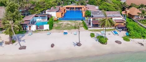 An aerial view of a resort with a swimming pool, beach, and multiple buildings.