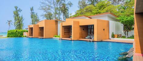 Zona junto a la piscina con vista despejada al océano, edificios de madera y abundante vegetación.