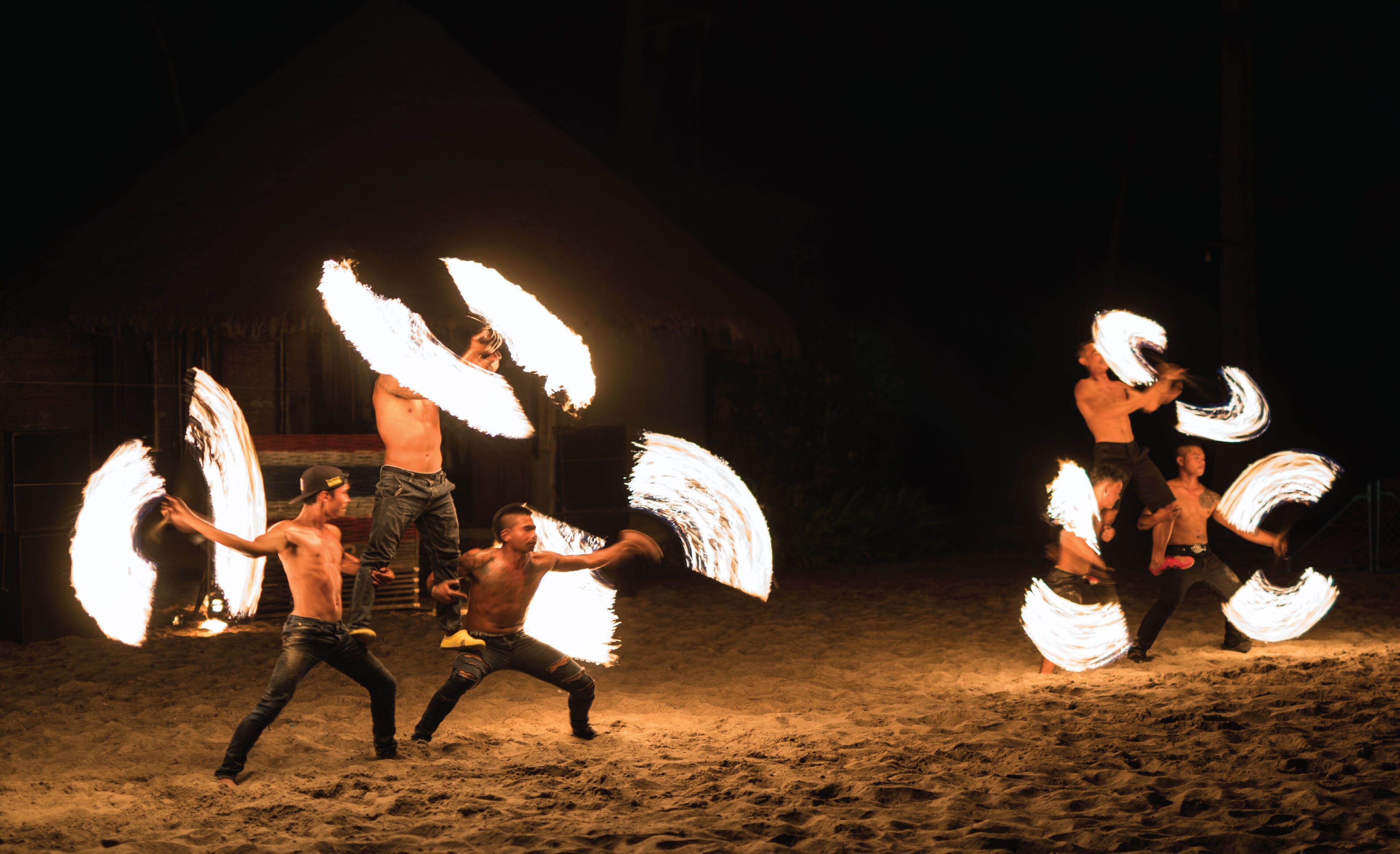 Un grupo de artistas con objetos de fuego en un entorno arenoso al aire libre.