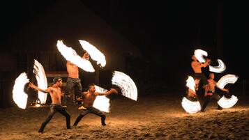 Un grupo de artistas con objetos de fuego en un entorno arenoso al aire libre.