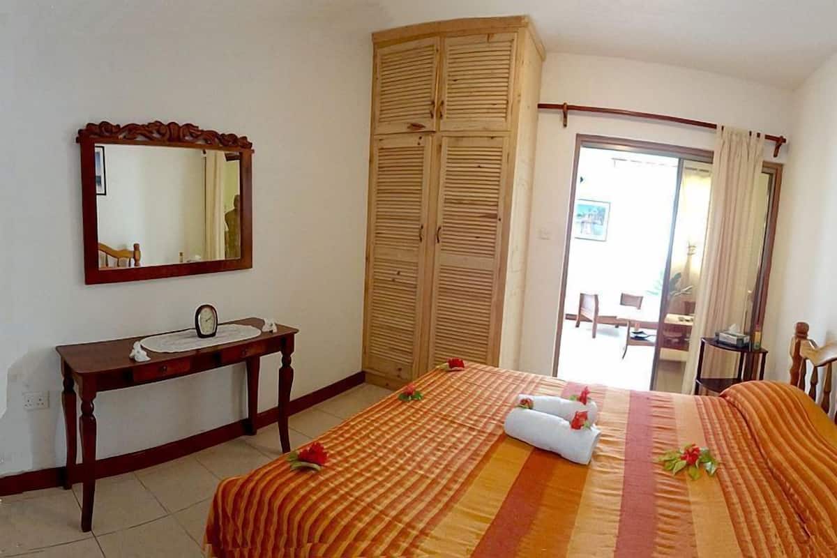 A hotel room with a bed, a bedside table with a mirror, a wooden wardrobe, and a view of the outside.