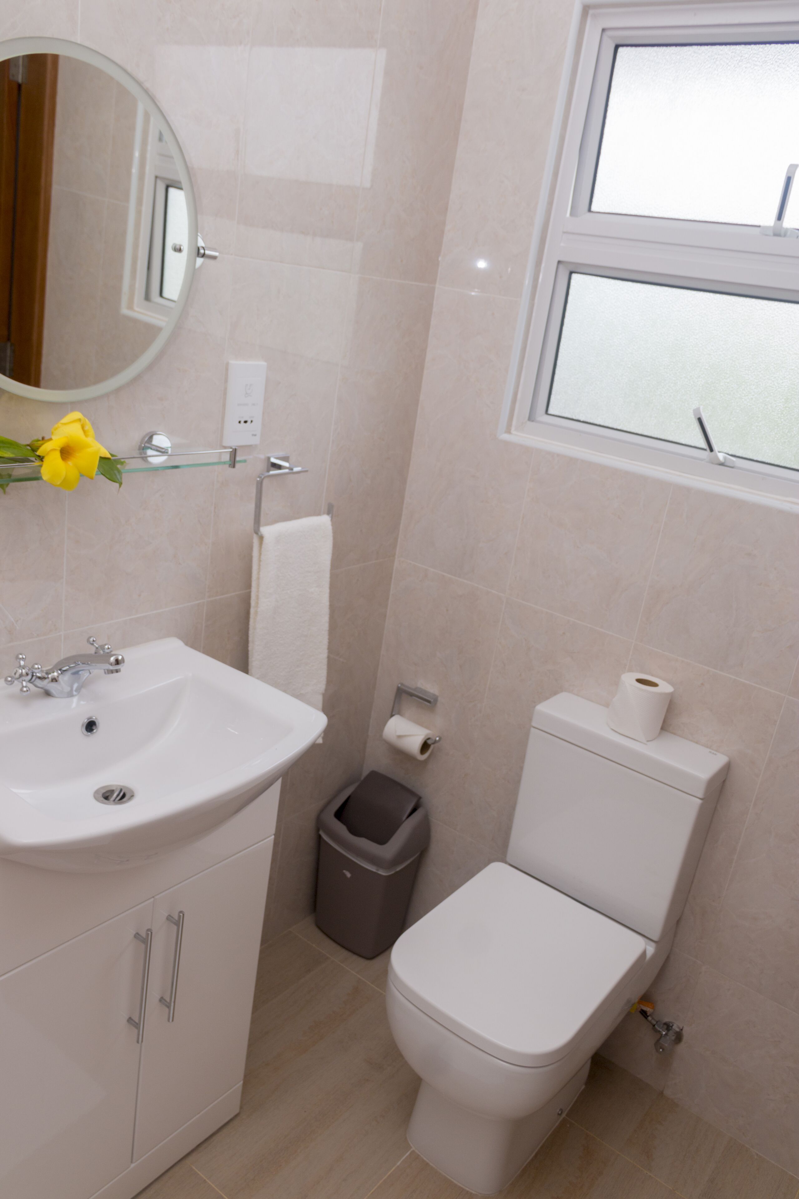Un baño con lavamanos blanco, espejo, inodoro y cubo de basura.
