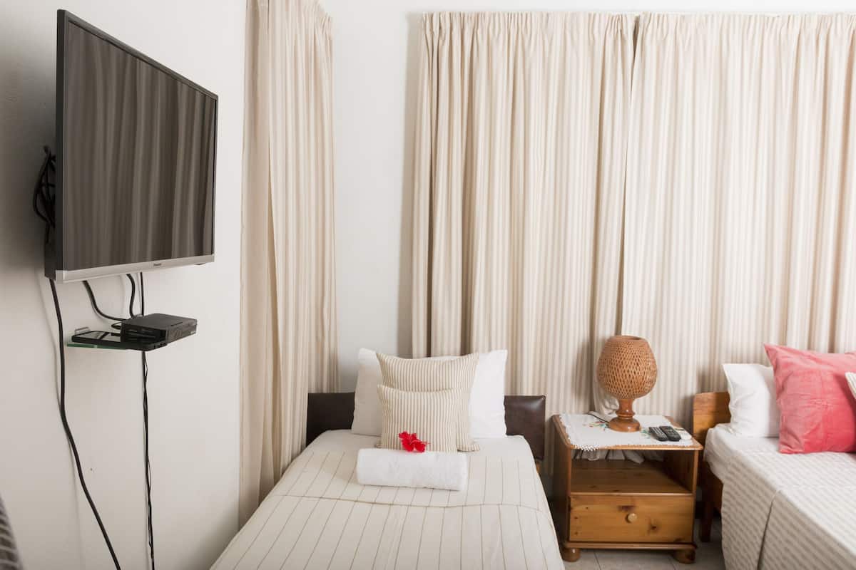 A hotel room with a bed, a bedside table with a lamp, a TV mounted on the wall, and a window with curtains.
