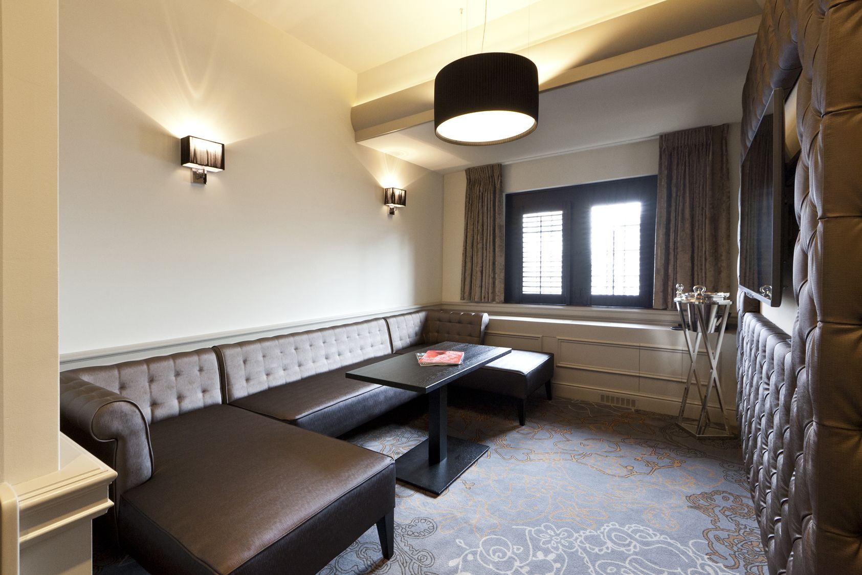A modern hotel room with a large window, a sofa, a small table, and a radiator.