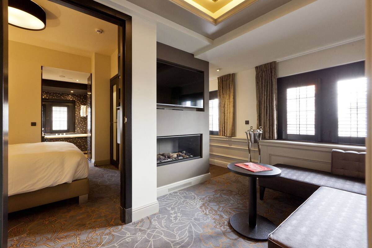 Une chambre d’hôtel avec un lit, une cheminée, un coin salon et une grande fenêtre.