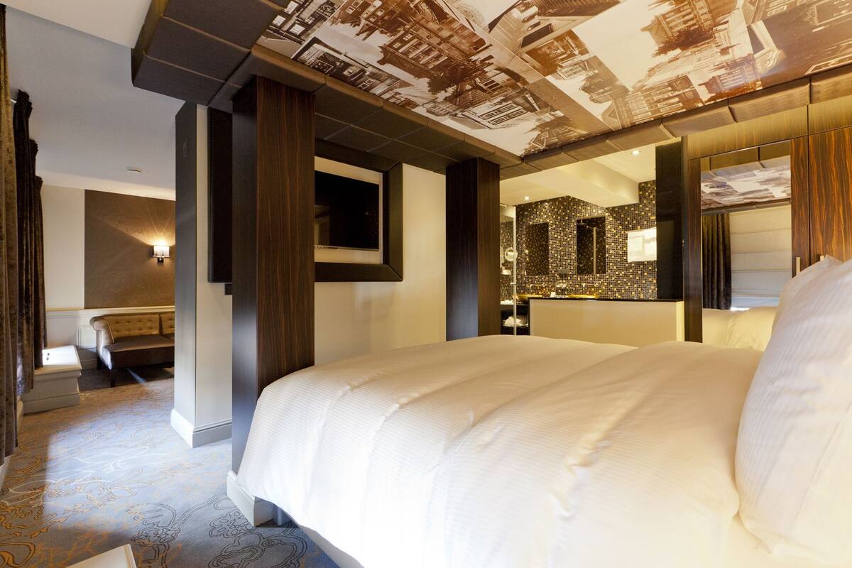Une chambre d’hôtel avec un grand lit, un coin salon avec un canapé, un miroir et un mur orné d’un motif en mosaïque.