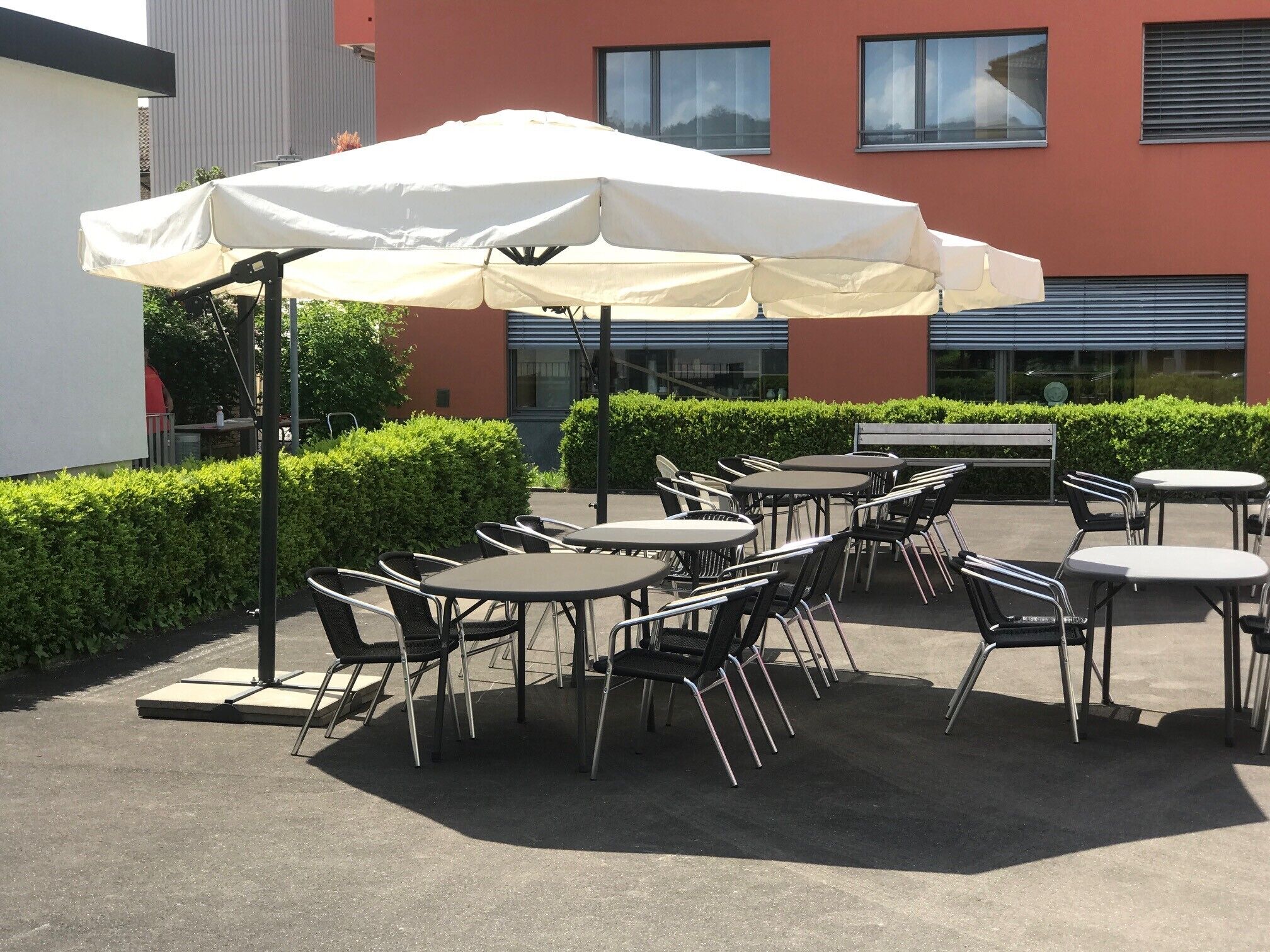 Une terrasse extérieure avec des tables et des chaises, un grand parasol et un bâtiment en arrière-plan.