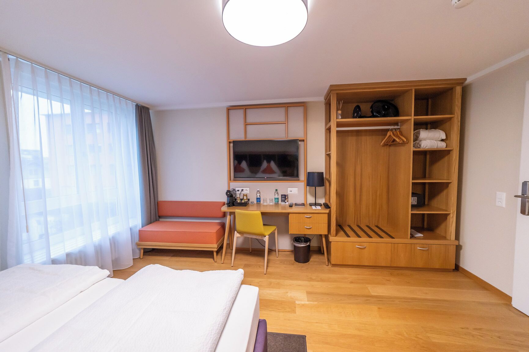 Een hotelkamer met een bed, een bureau, een stoel, een televisie, een kledingkast en een raam met gordijnen.