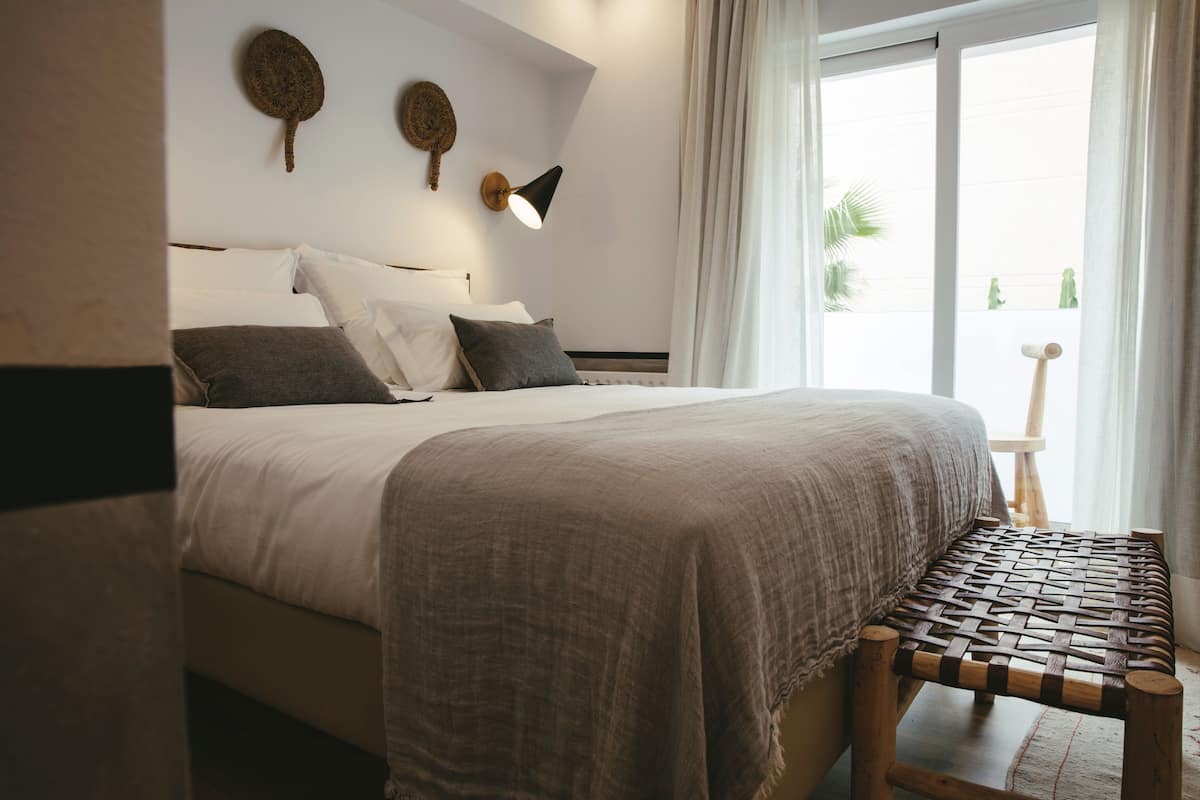 A bedroom with a bed, a bedside table, a lamp, and a view of the outdoors.