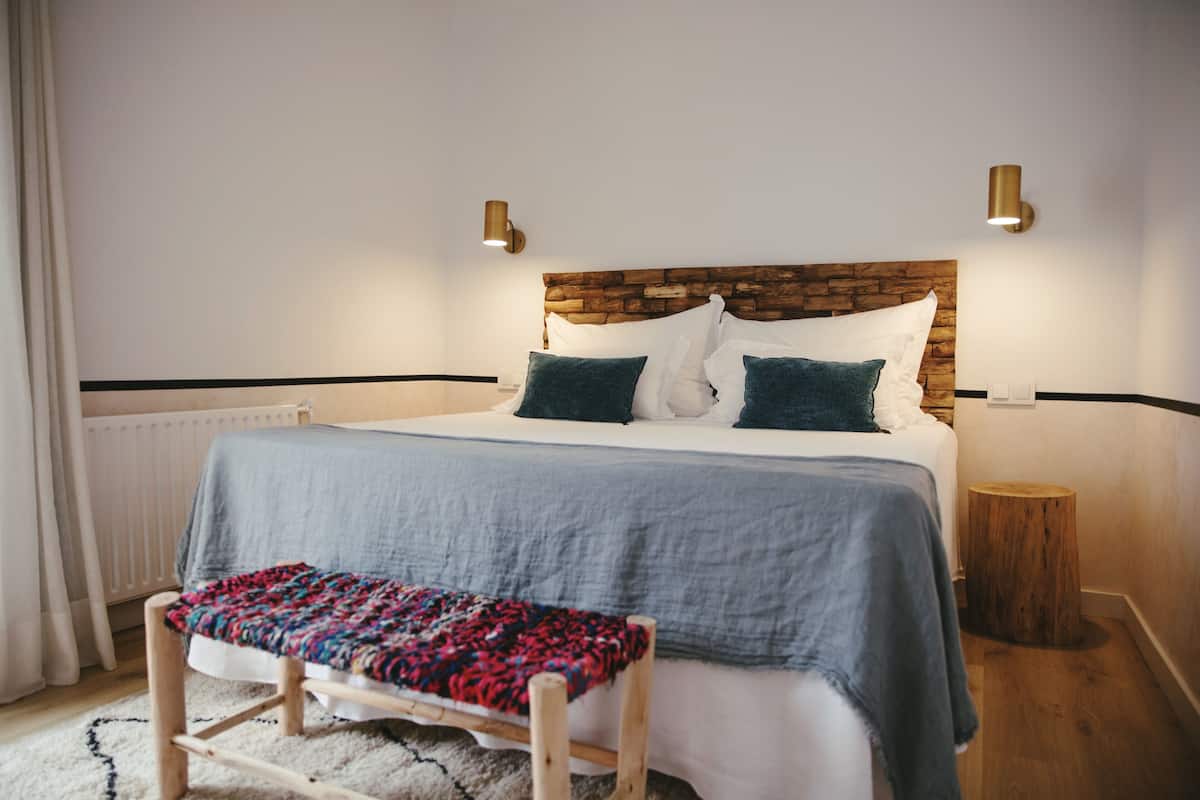 A neatly arranged bedroom with a wooden headboard, a bench, and two wall-mounted lights.