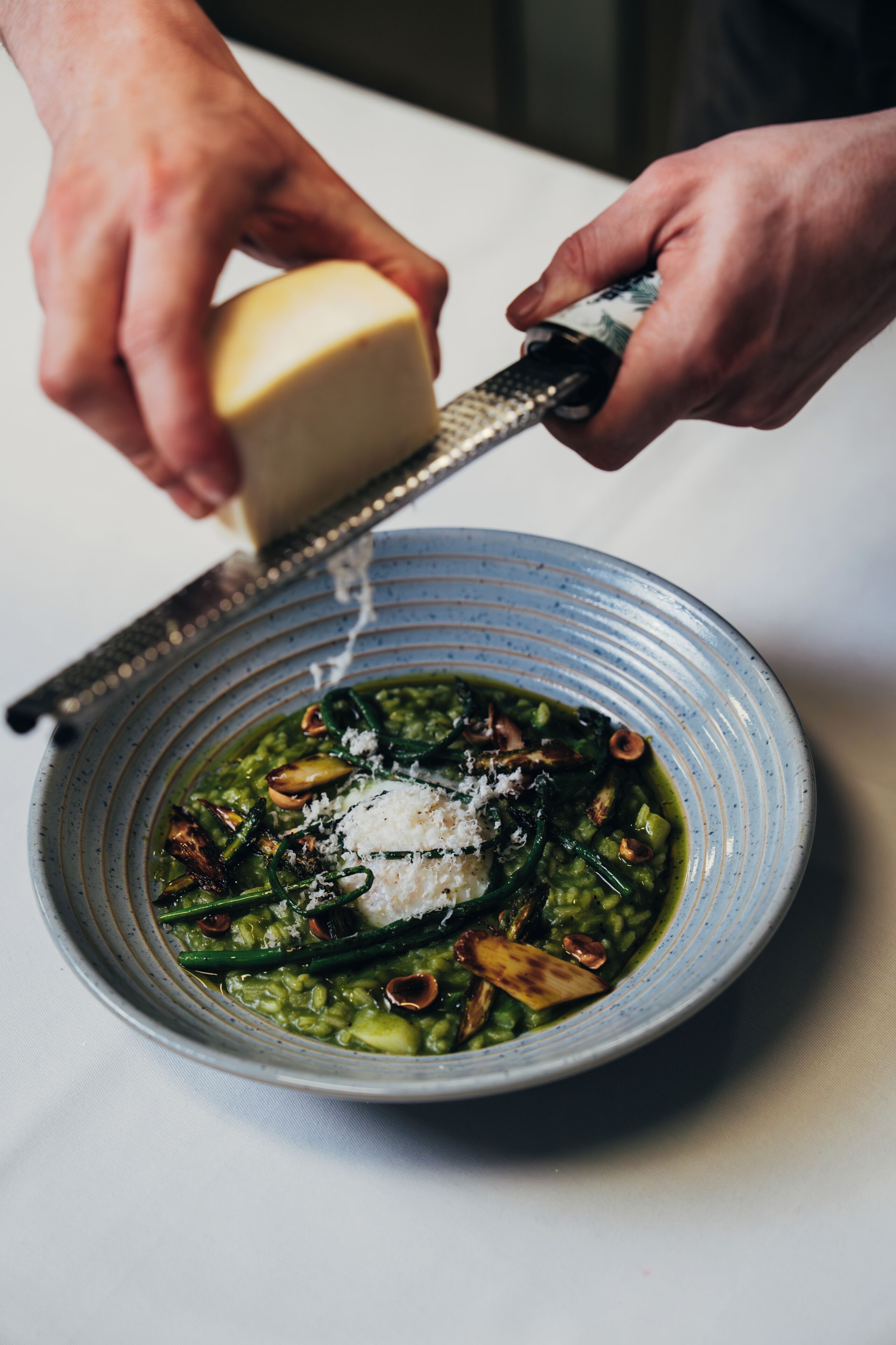 Una persona ralla queso sobre un plato de pasta con verduras verdes.