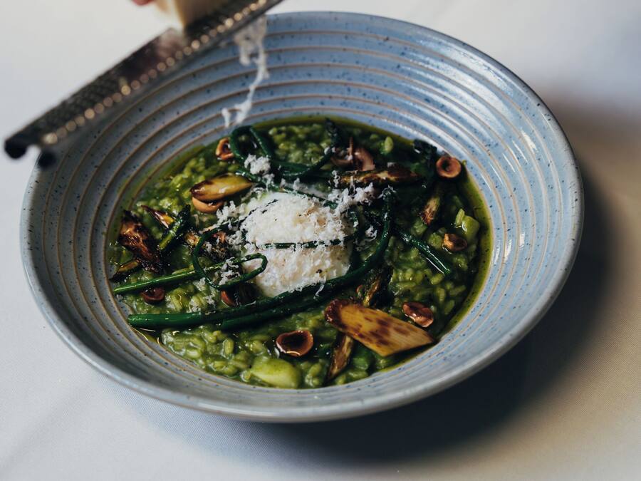 Una persona ralla queso sobre un plato de pasta con verduras verdes.