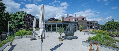 Un patio al aire libre con asientos, sombrillas y una gran escultura abstracta.