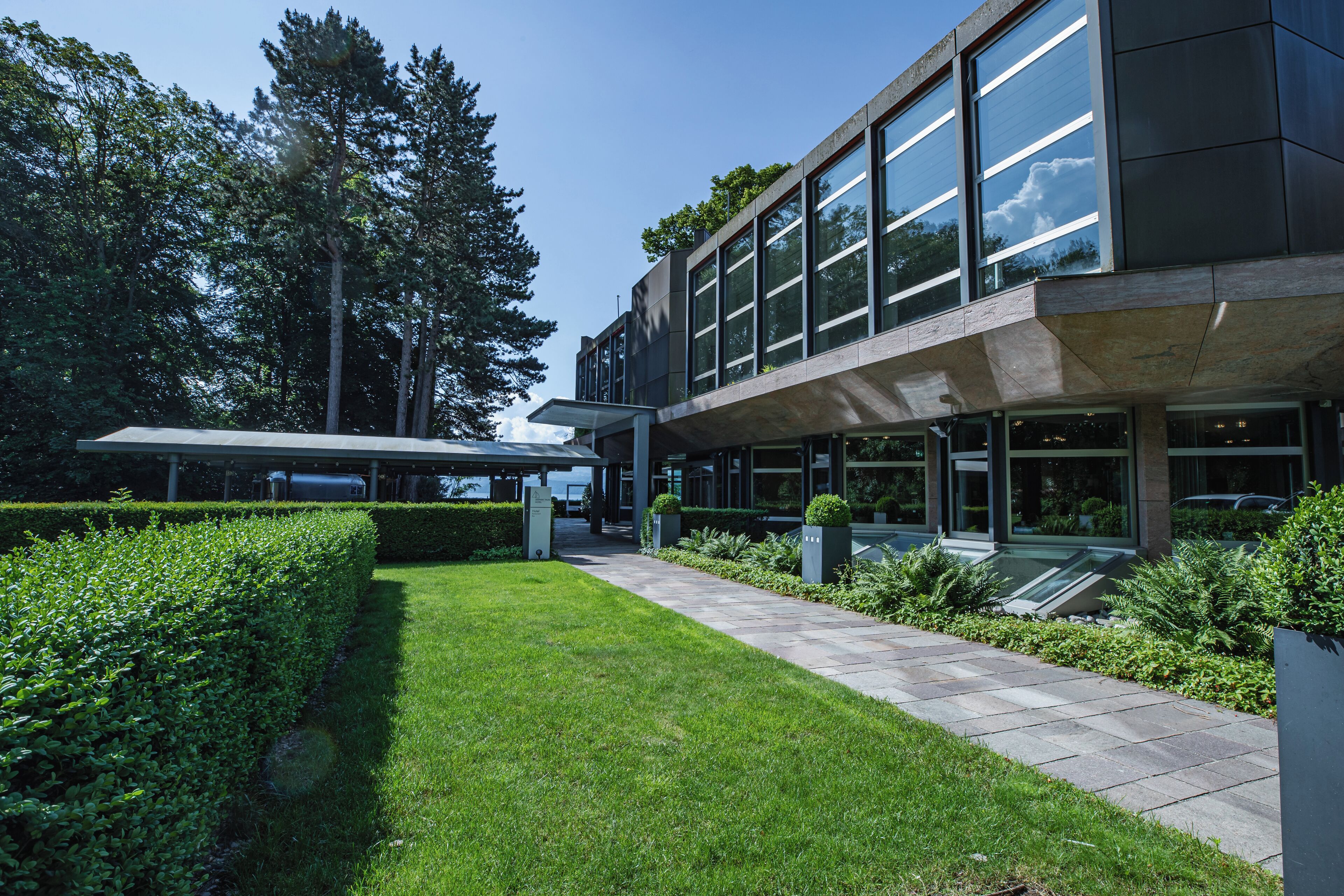 Un bâtiment moderne doté de grandes fenêtres, d’une allée couverte et d’un aménagement paysager bien entretenu.