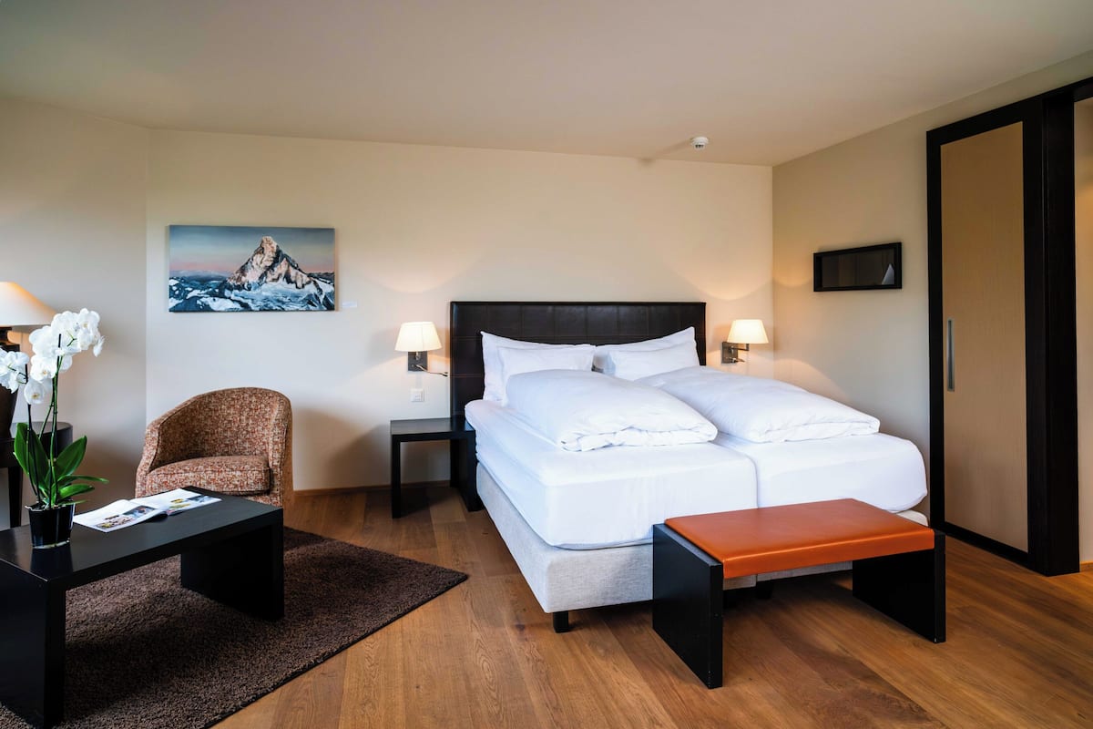 A hotel room with a bed, a chair, a small table, and a painting on the wall.