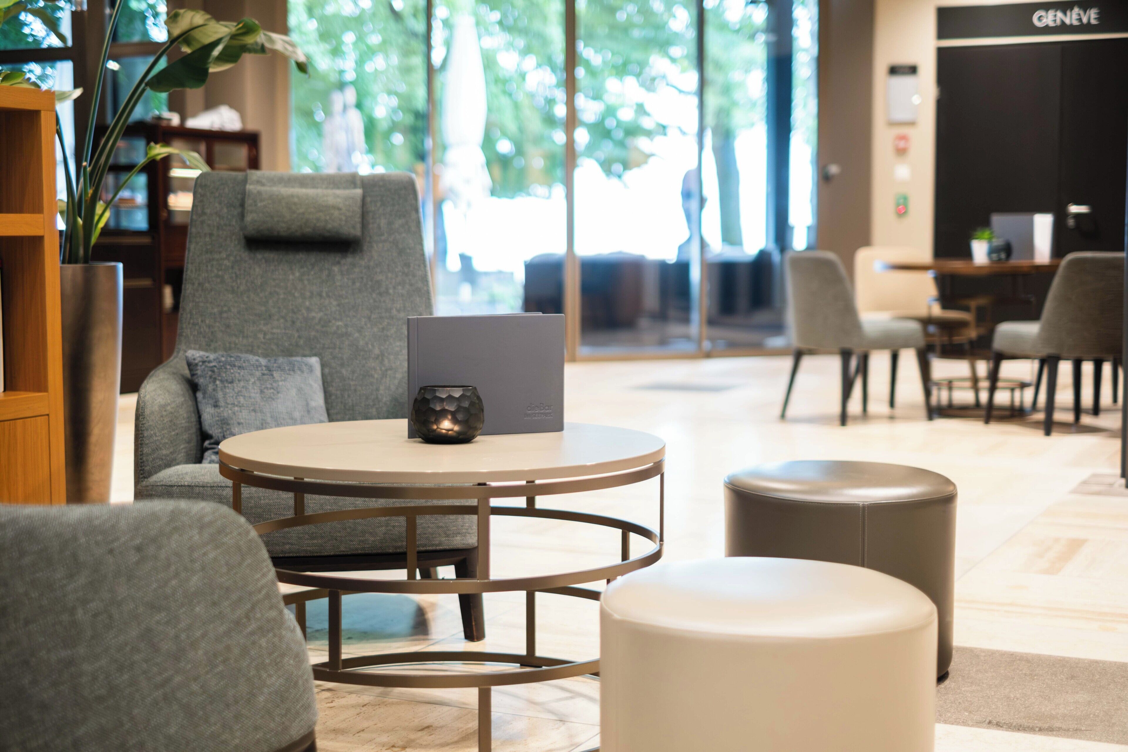 A modern lounge area with a round table, grey armchairs, and a laptop on the table.
