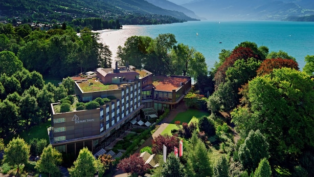 A modern hotel with a rooftop terrace, surrounded by lush greenery and a lake view. - Hotel Seepark Thun (Thun)