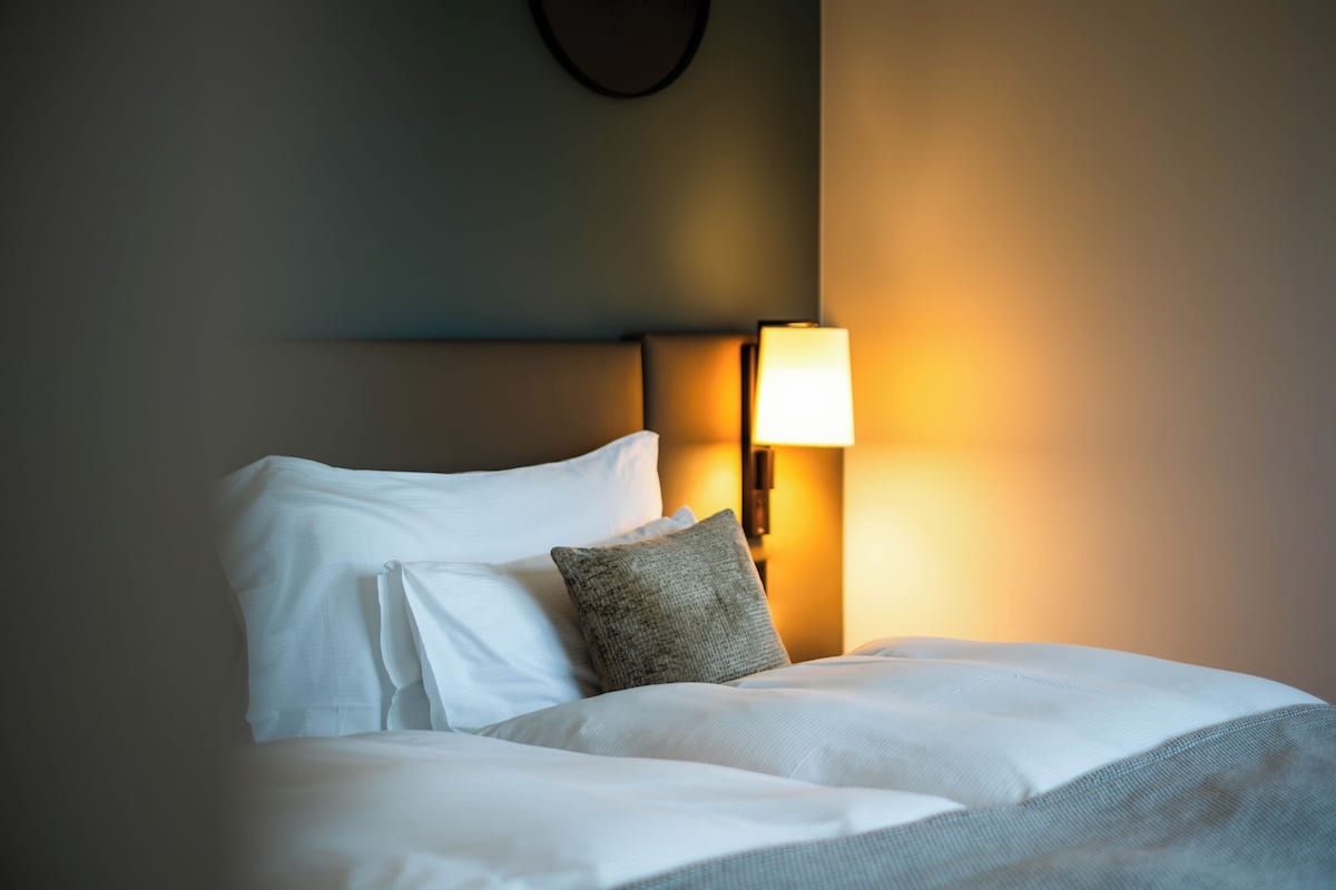 A neatly made bed with white linens and a single gray pillow.