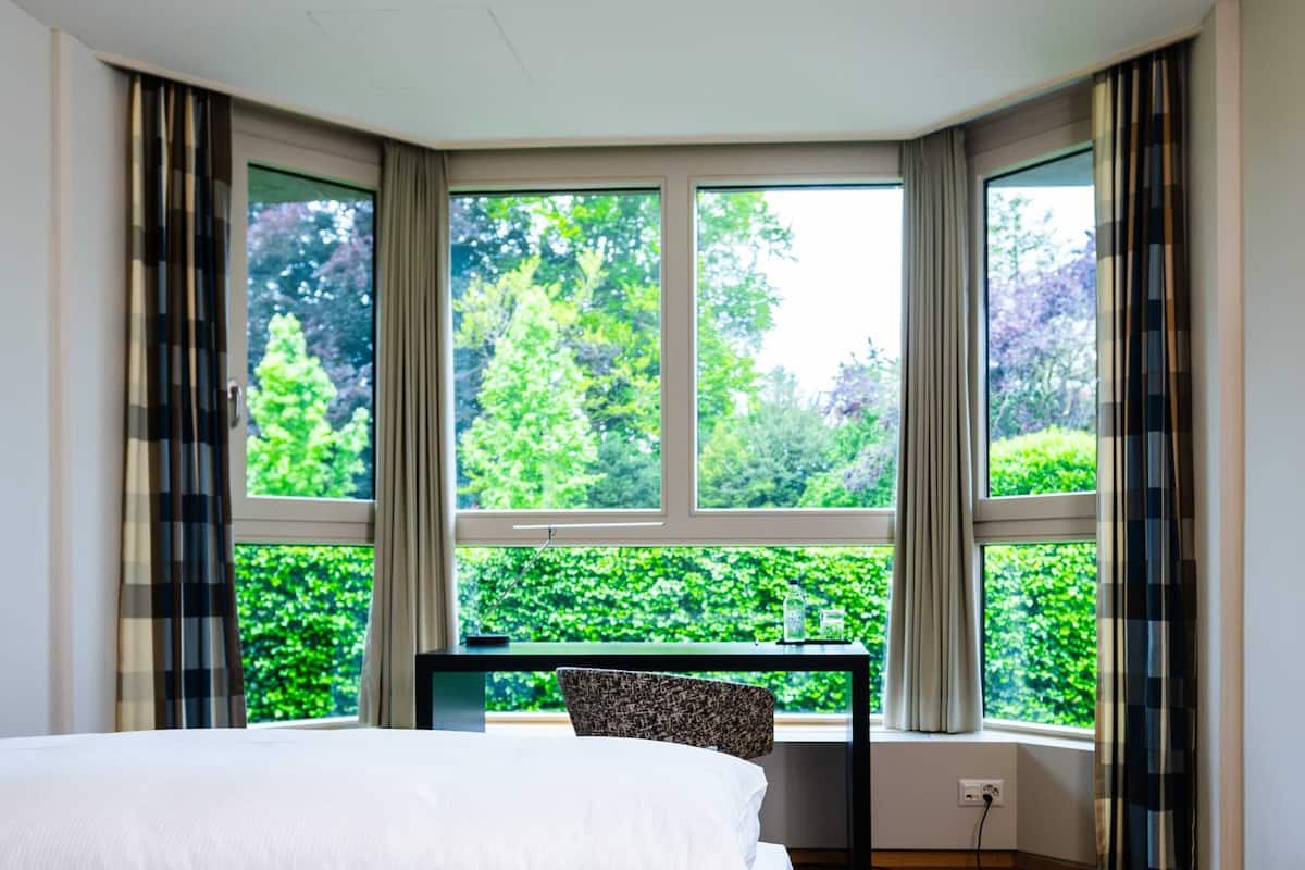 A bedroom with a large window, a bed, a chair, and a small table.