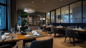 A modern restaurant with wooden tables, grey upholstered chairs, and a large chandelier. - Hotel Seepark Thun (Thun)