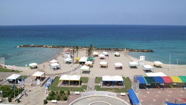 A beachside area with multiple colorful tents and a paved walkway leading to the sea. - Madison Hotel Nahariya (Nahariya)