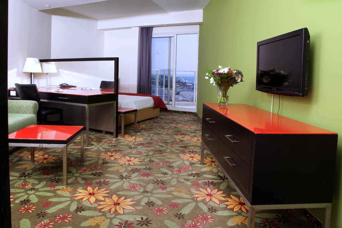 A hotel room with a bed, a desk, a chair, a dresser, a television, and a window with a view.