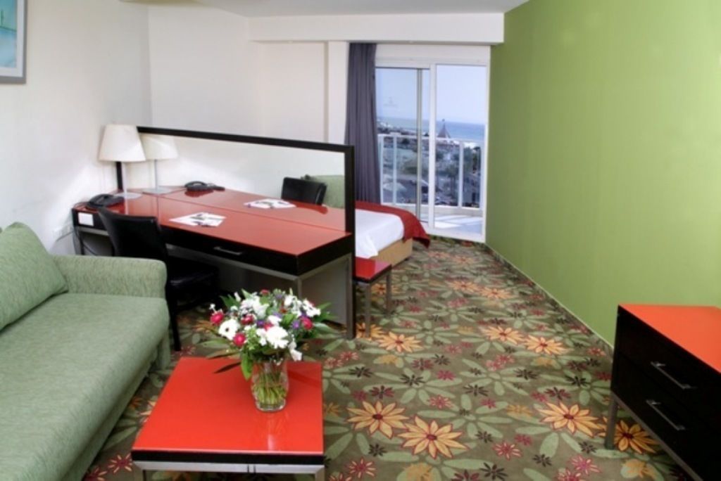 A hotel room with a bed, a desk, a chair, a sofa, and a window with a view of the city.