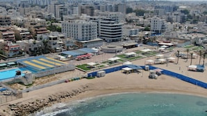 An urban beach area with a swimming pool, beach umbrellas, and a sandy shoreline. - Madison Hotel Nahariya (Nahariya)