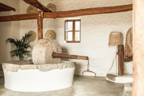 A rustic interior with a stone mill, wooden beams, a window, and woven hats on the wall. - Casa Maca Hotel (Ibiza Town)