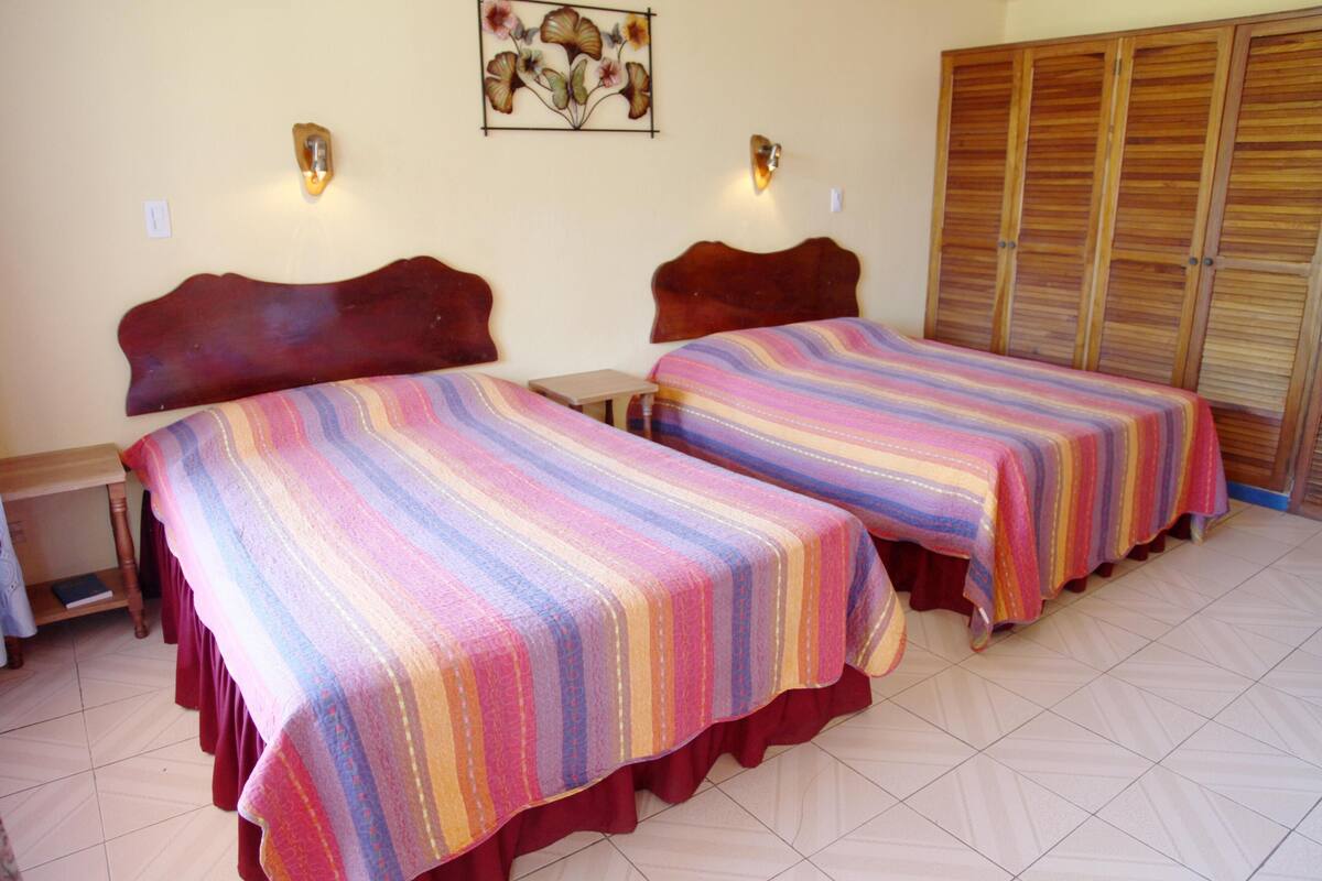 Duas camas com roupa de cama listrada, um guarda-roupa de madeira e uma pequena mesa.