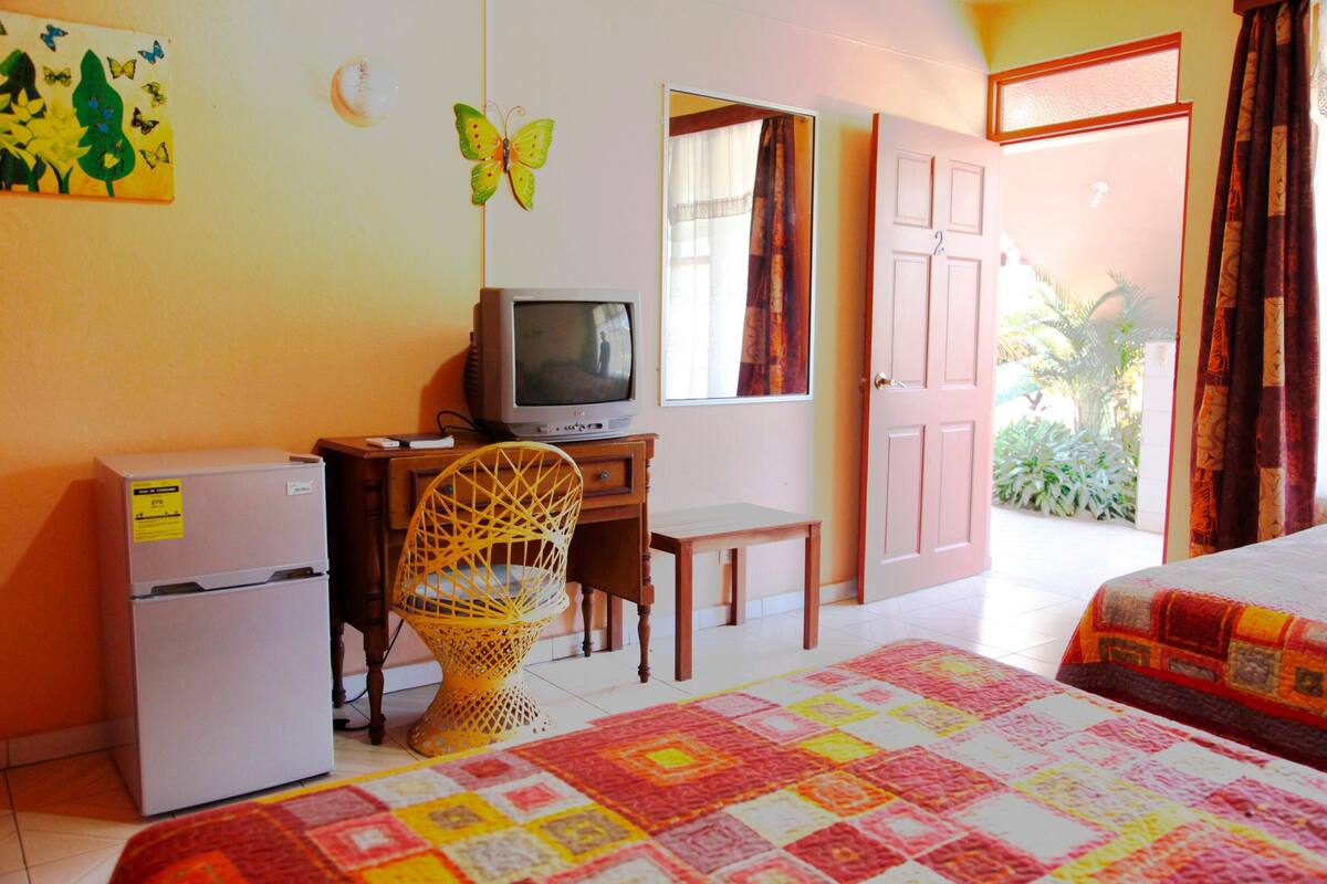 Quarto com cama, televisão, frigorífico, cadeira e janela com cortinas.
