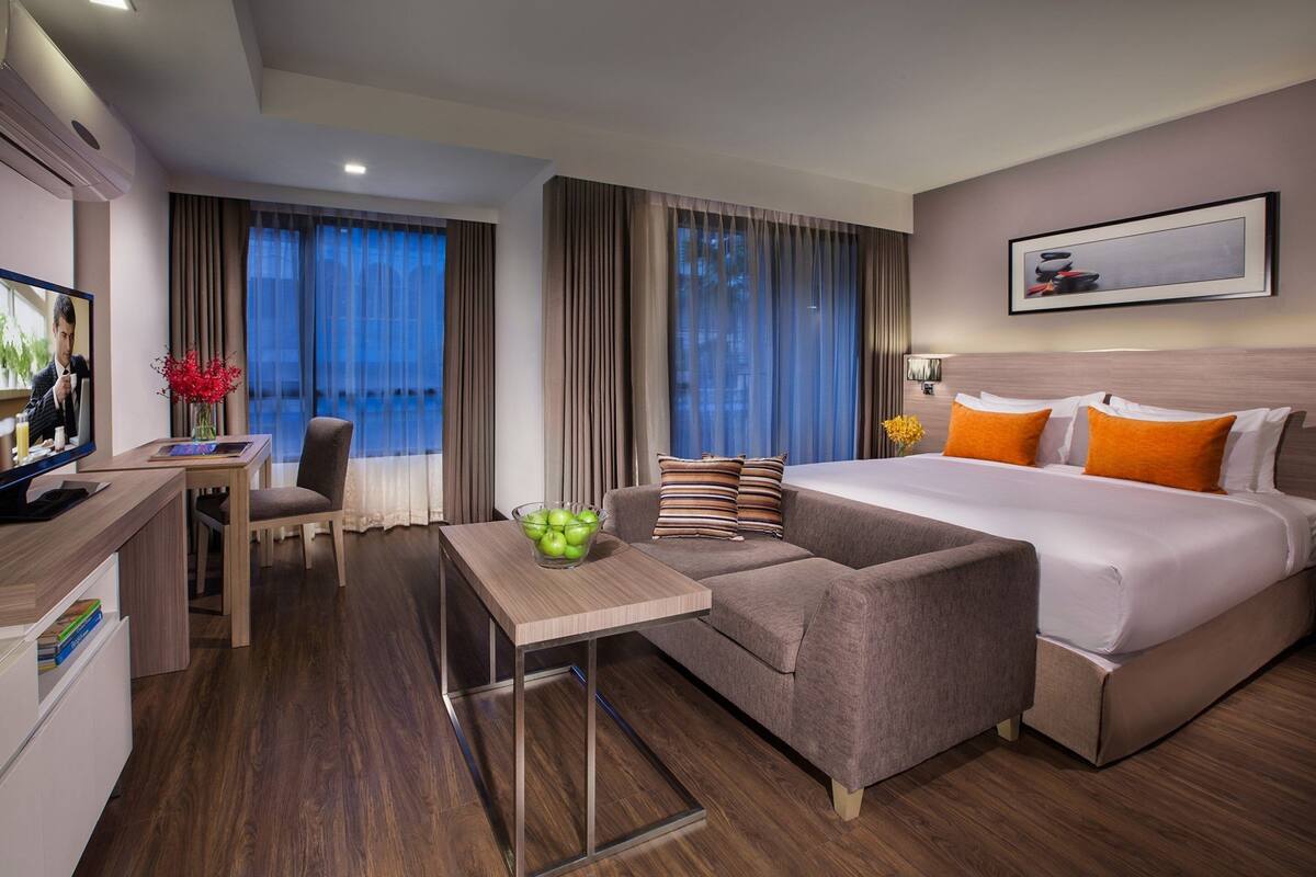 A modern hotel room with a bed, a sofa, a desk, and a TV.