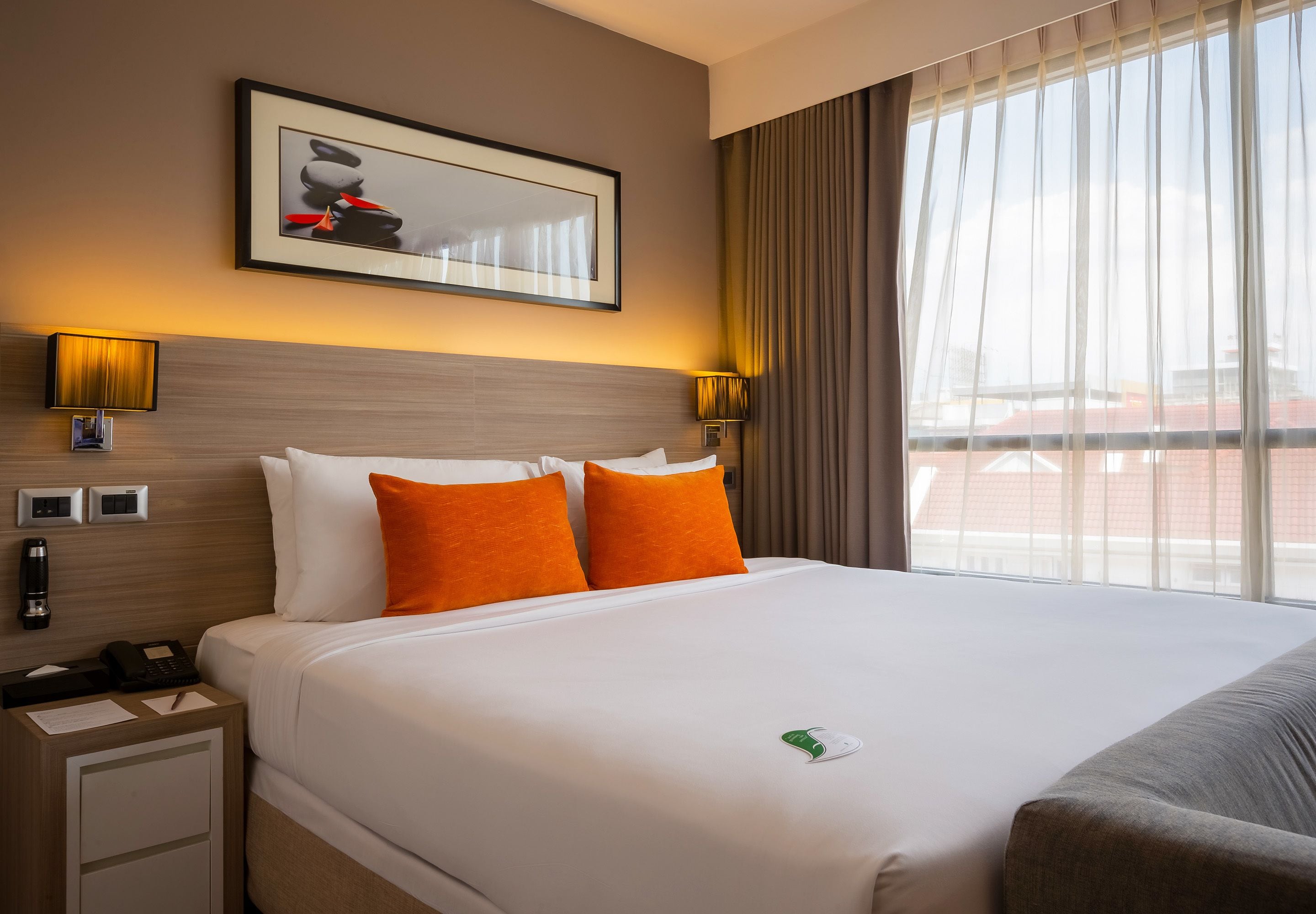 A hotel room with a large bed, two bedside lamps, a framed picture on the wall, and a window with curtains.