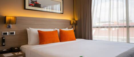 A hotel room with a large bed, two bedside lamps, a framed picture on the wall, and a window with curtains.