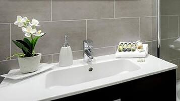 Un baño con lavamanos blanco, una orquídea en maceta, un dispensador de jabón y una bandeja con artículos de aseo.