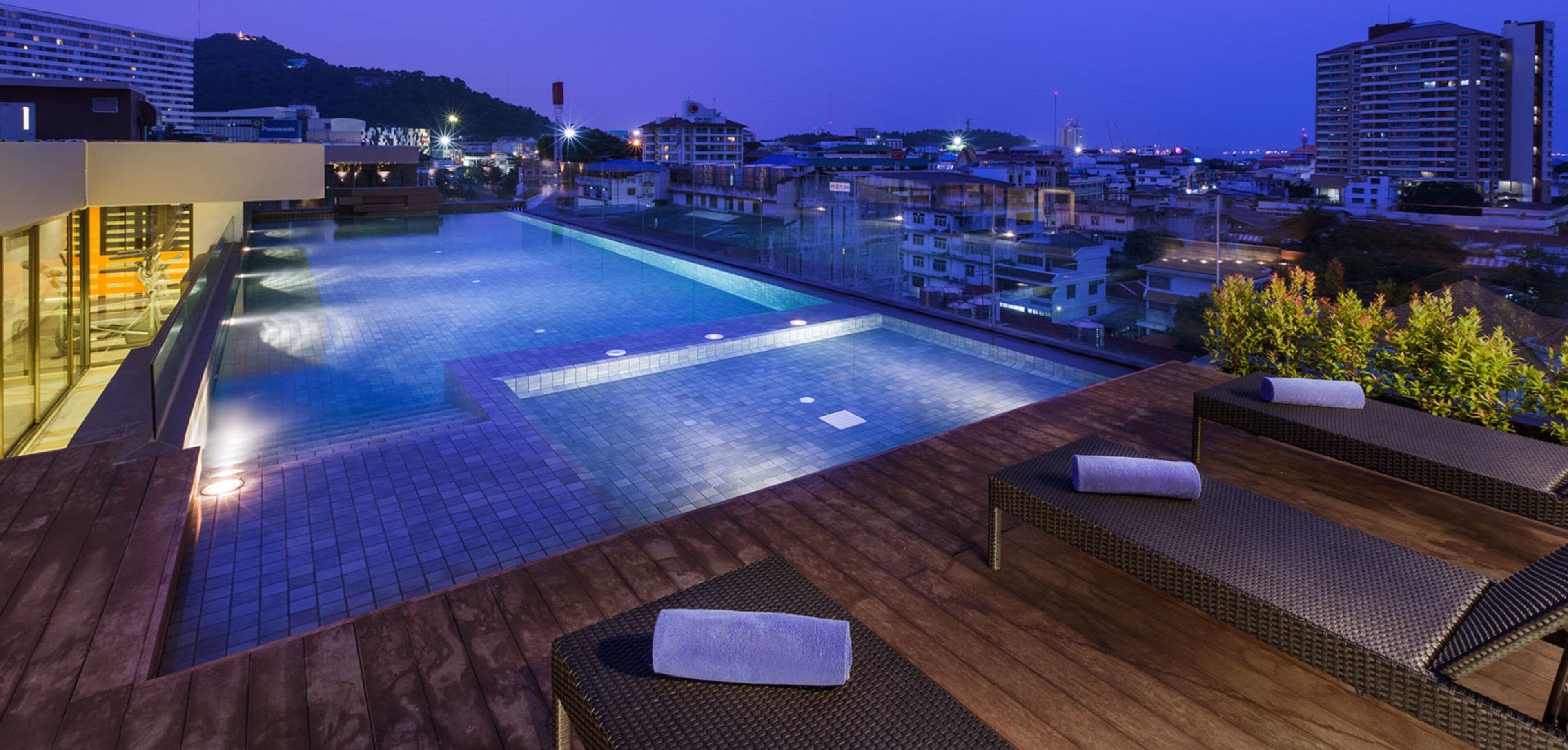 A rooftop pool area with lounge chairs and a view of the cityscape at dusk.