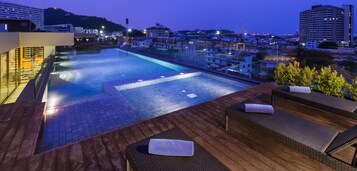 A rooftop pool area with lounge chairs and a view of the cityscape at dusk.