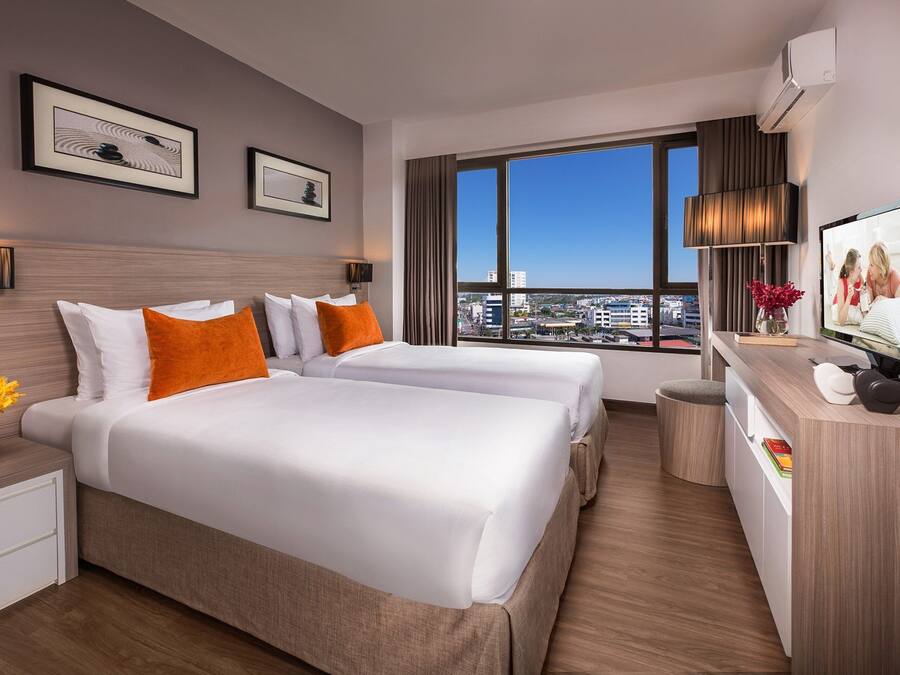 A hotel room with two beds, a desk, a TV, and a large window with a city view.