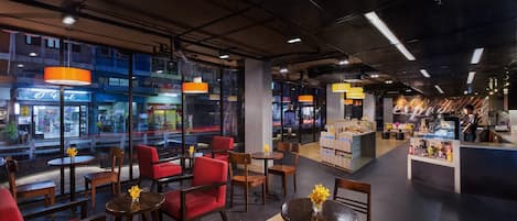 A modern cafe with red chairs and tables, a counter with a display, and large windows overlooking a busy street.