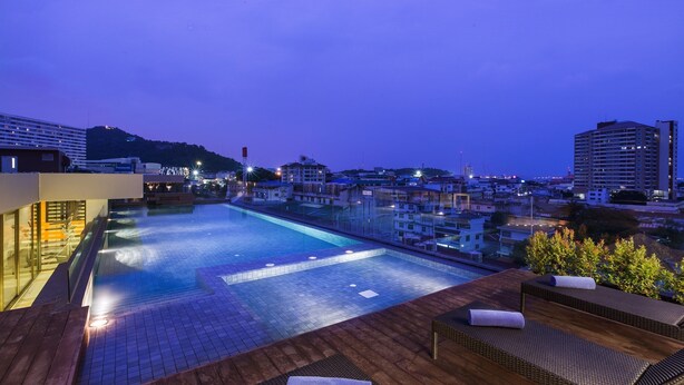 Ein Pool auf dem Dach mit Liegestühlen und Blick auf die nächtliche Skyline.