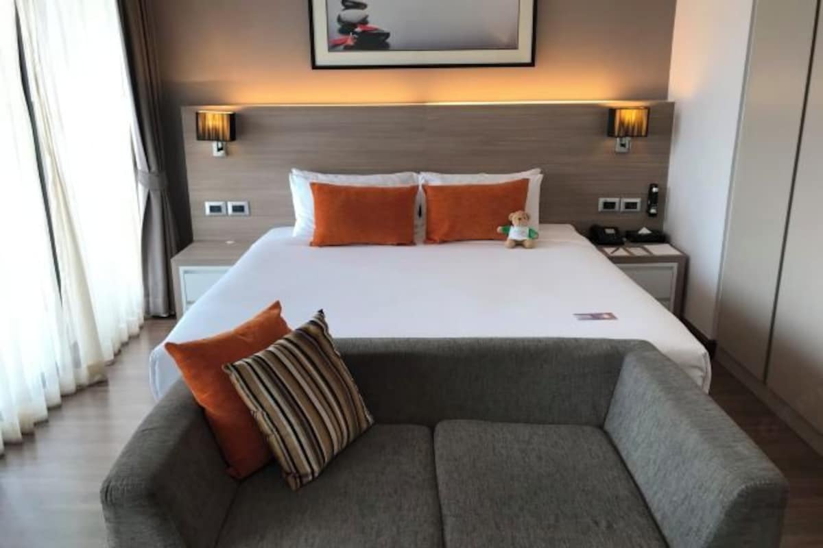 A hotel room with a large bed, two nightstands, a sofa, and a wall-mounted lamp.