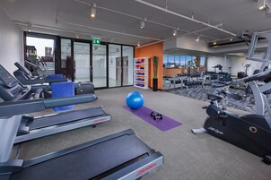 Un gimnasio con cintas de correr, una pelota de ejercicio, mancuernas y máquinas de pesas.