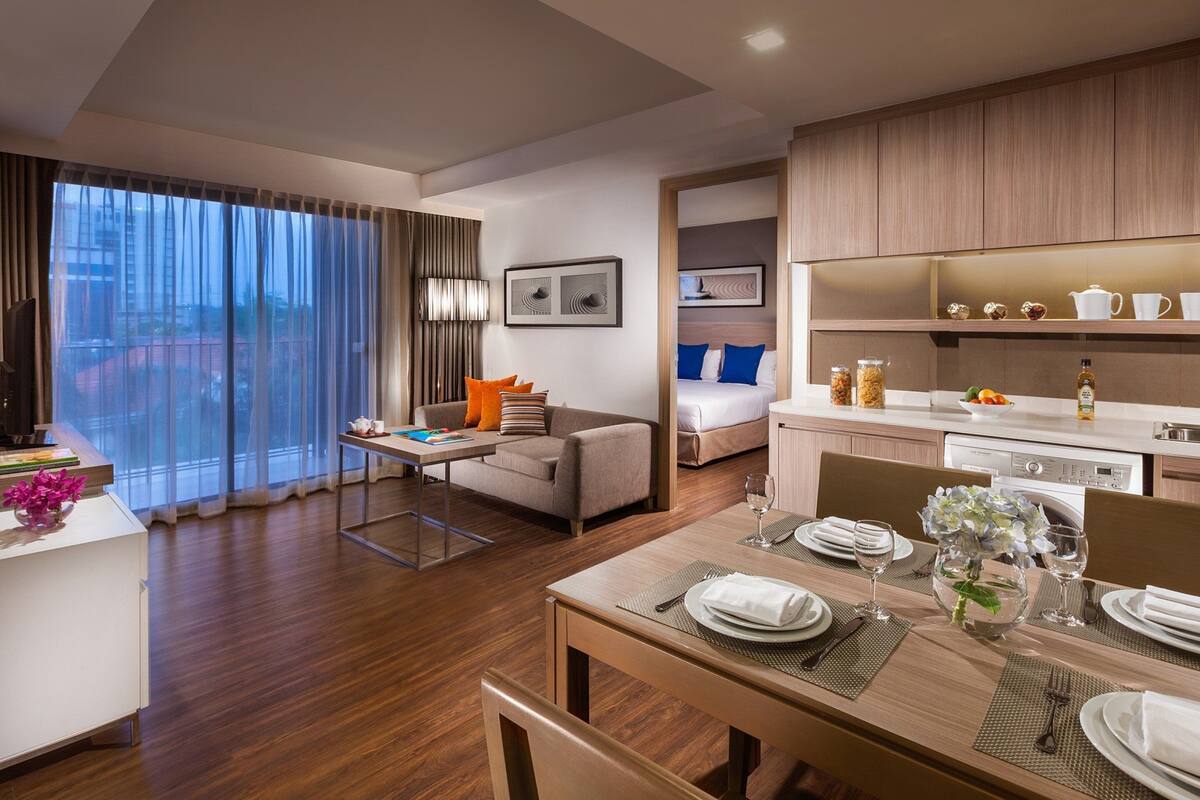 A modern hotel room with a dining area, a sofa, a bed, and a kitchen area.